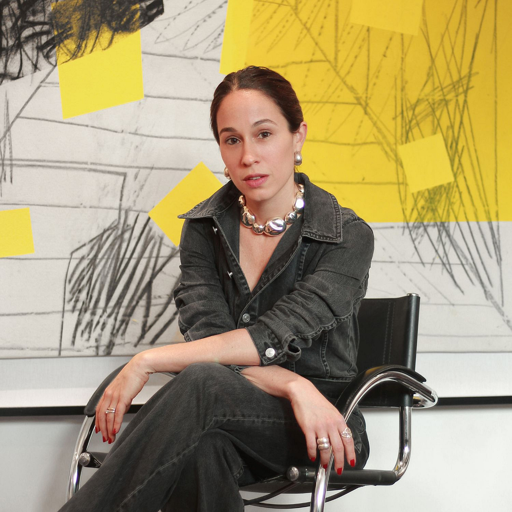 Ana Volante sentada con una obra de arte amarilla, negra y gris