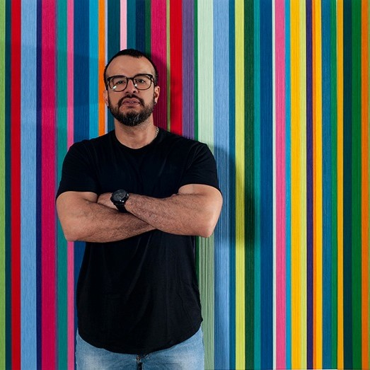 Reymond Moreno parado y en el fondo una de sus obras coloridas de arte cinético