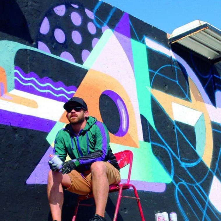 Dagor sentado junto a una de sus obras pintadas en una pared de una calle